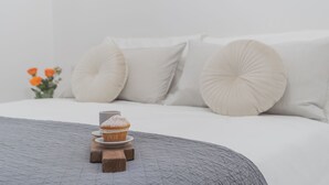 A neatly made bed with a grey quilt, a wooden stand holding a cupcake, and a vase with orange flowers on the side. - Luce Apartment in Como (Como)