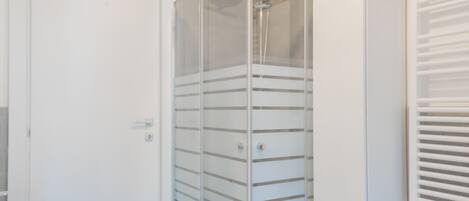 A modern bathroom with a glass-enclosed shower, a white sink, and a cabinet with a plant on top.