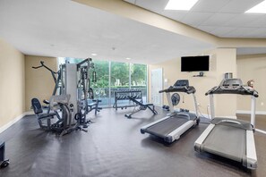 Une salle de sport équipée de tapis de course, d’appareils de musculation et d’un téléviseur fixé au mur.