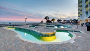 Et poolområde med flere swimmingpools, et nedsænket loungeområde og havudsigt i solnedgang.