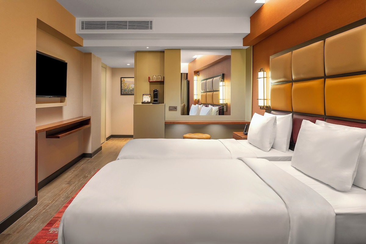 Una habitación de hotel con una cama grande, un televisor, un espejo y una mesita.