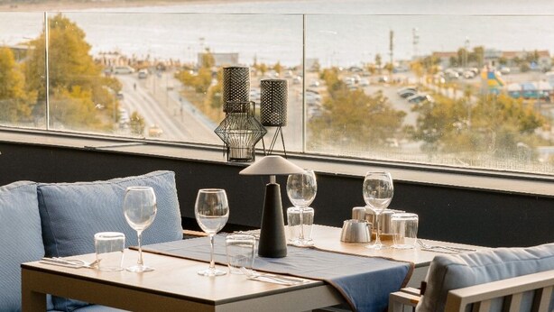 A dining area with a table set for two, a view of the water, and a cityscape in the background.