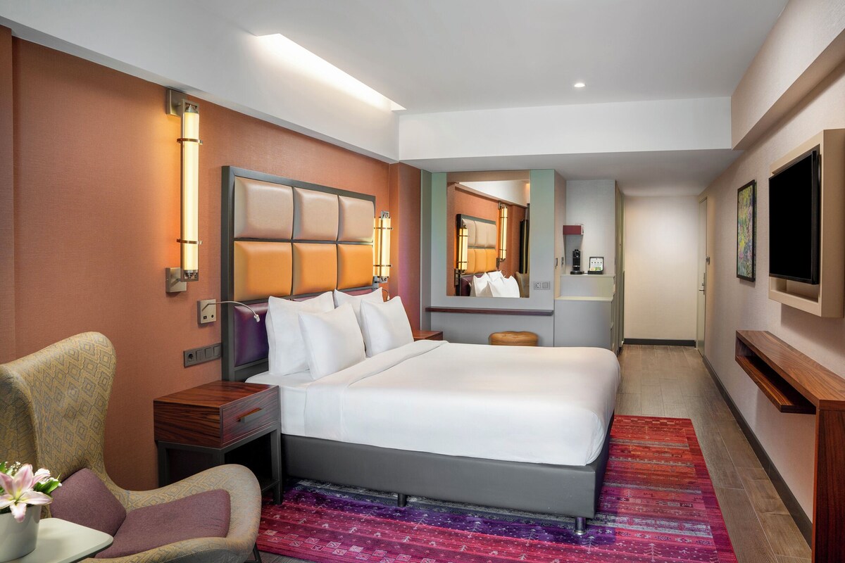 Una habitación de hotel con una cama grande, una silla, un escritorio, un televisor y un espejo.