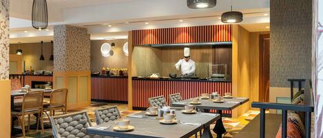 A restaurant with a chef preparing food, tables with chairs, and a bar area.