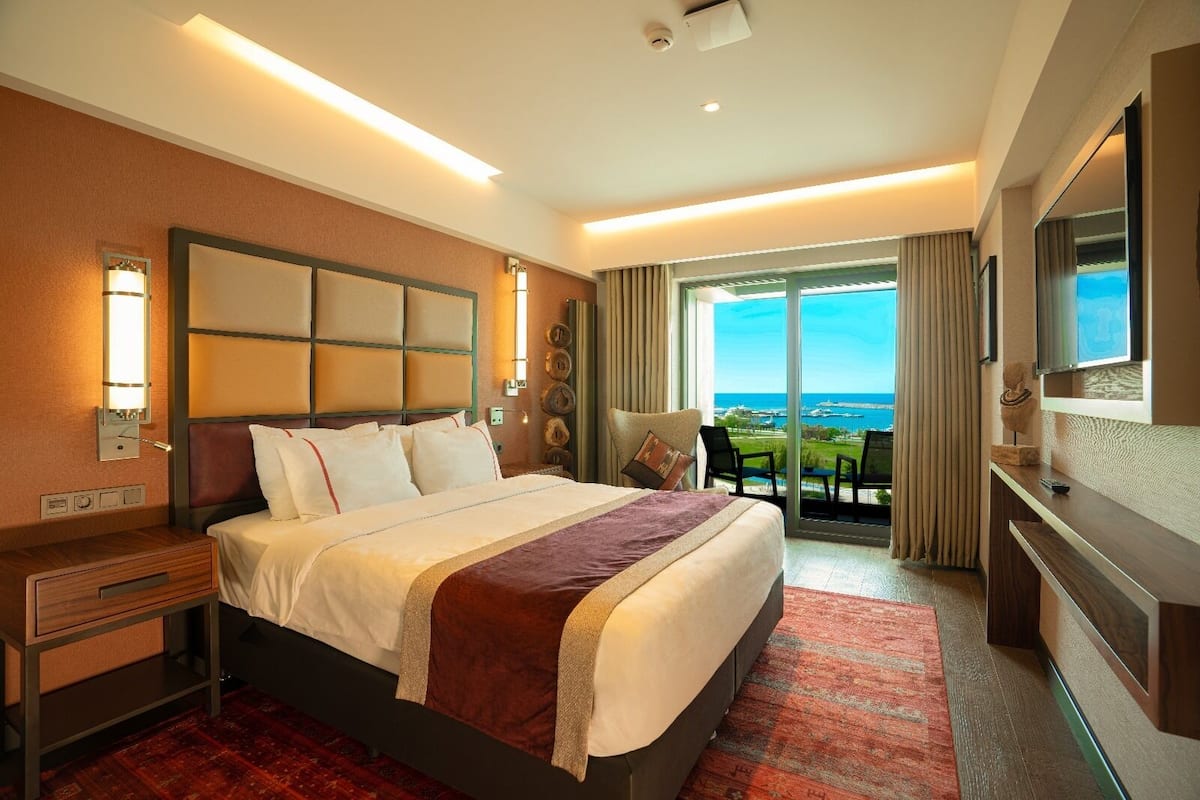 Ein Hotelzimmer mit einem großen Bett, einem Schreibtisch, einem Fernseher und Meerblick.