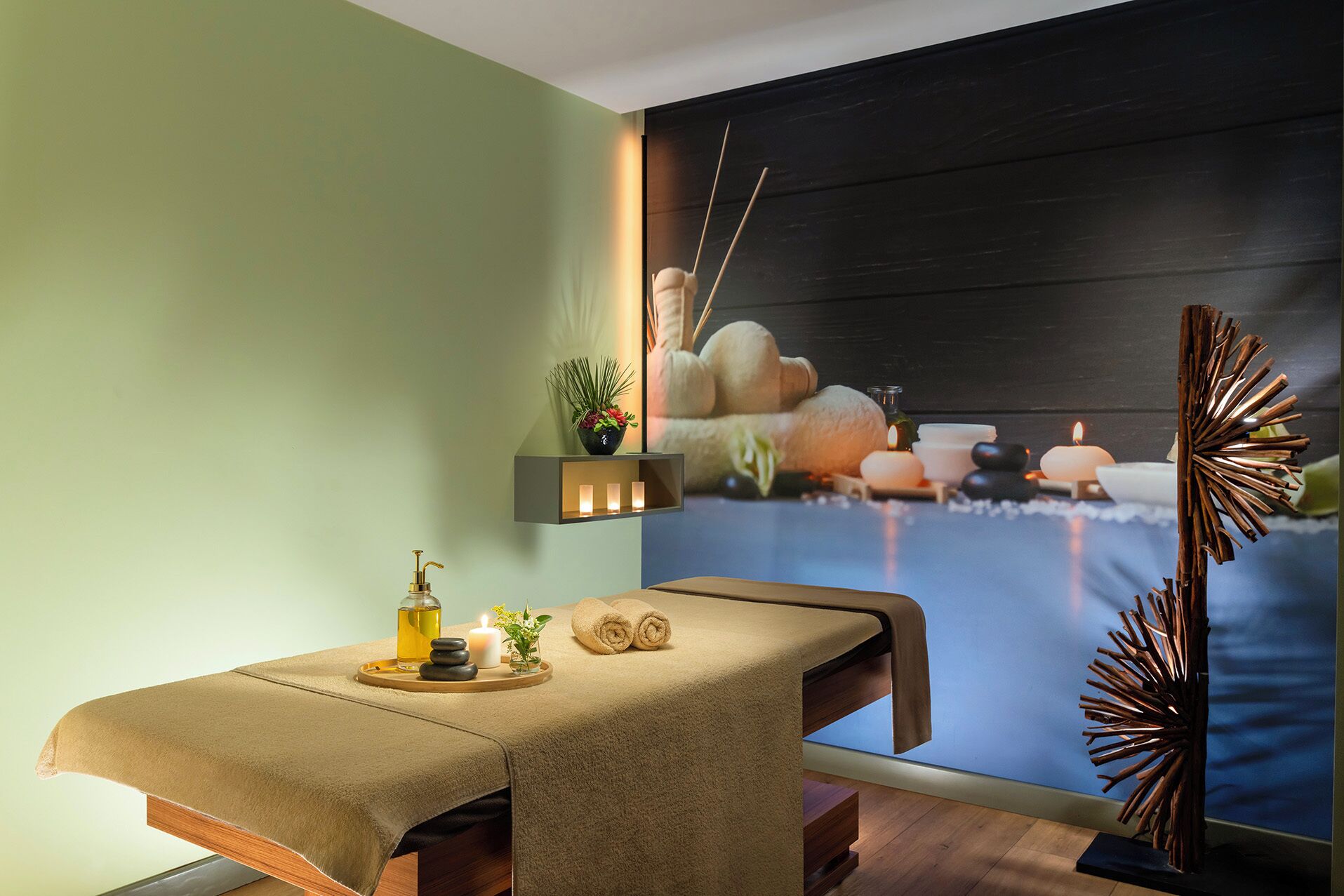 Un cuarto de spa con una camilla de masaje, un estante de pared con velas y un adorno mural.