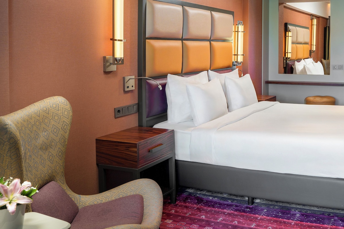 Una habitación de hotel con una cama grande, una mesita de noche, una silla, un aparador y un espejo.