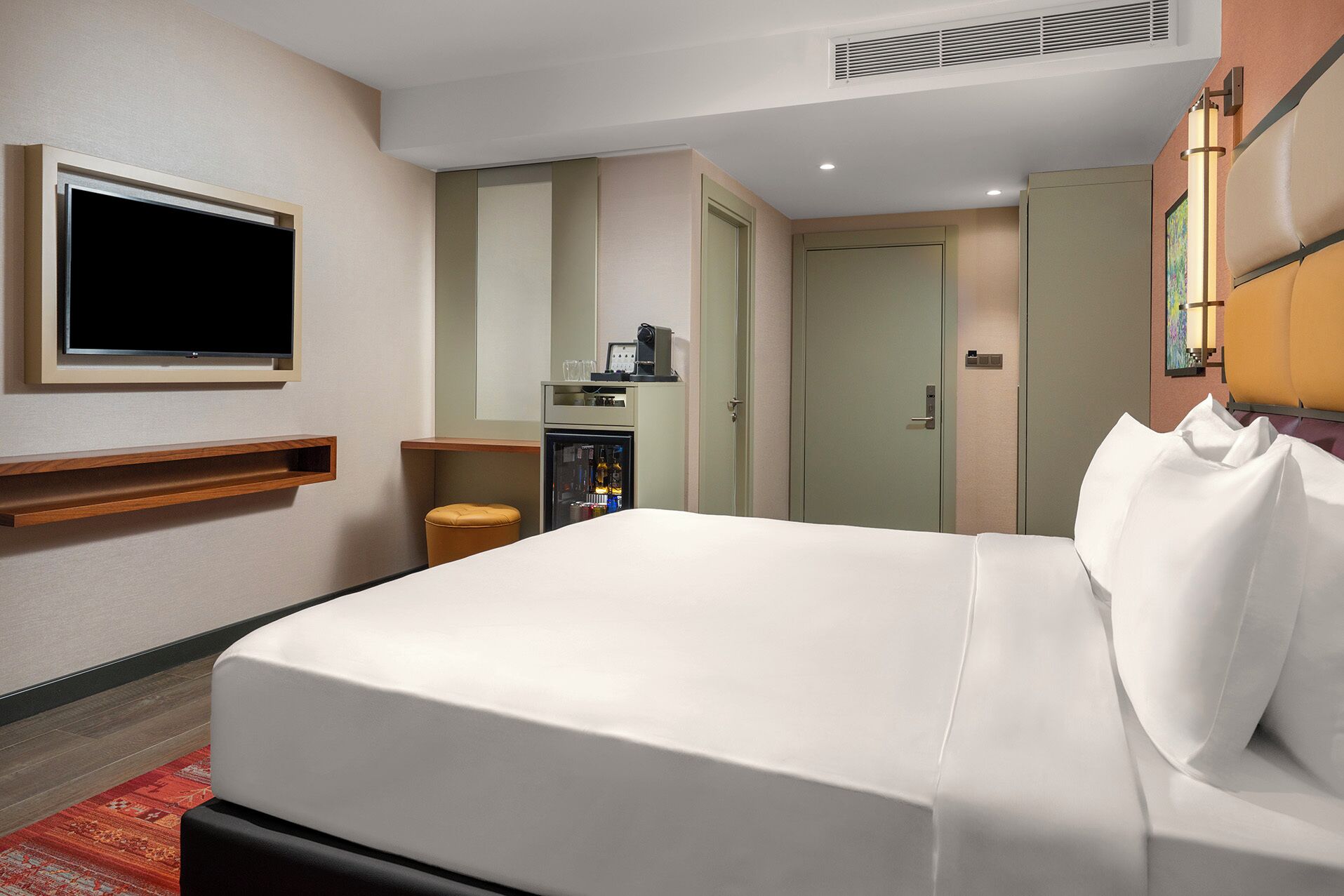 A hotel room with a bed, a television, a minibar, and a door.