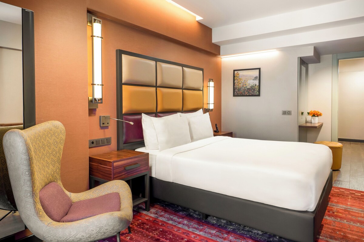 Una habitación de hotel con una cama, una silla, una mesita de noche y una lámpara de pared.