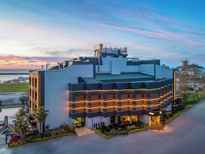 Un hotel moderno con terraza en la azotea, un letrero llamativo y un acceso arbolado.