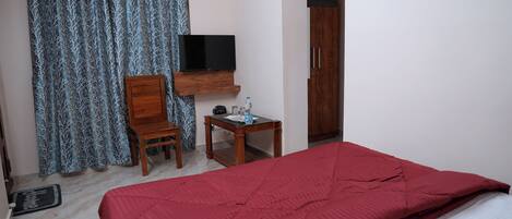 A room with a bed, a television on a wooden shelf, a small table with a bottle, and a wardrobe.