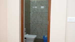 Un baño con inodoro, un cubo azul y una pared de mármol.