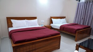 Habitación de hotel con dos camas de madera, cada una con ropa blanca y una colcha roja. Hay una mesita de madera y una silla en la habitación.