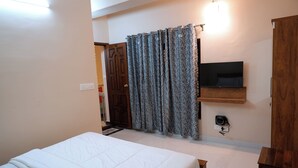Un dormitorio con una cama, un televisor en la pared, un armario de madera y una cortina.