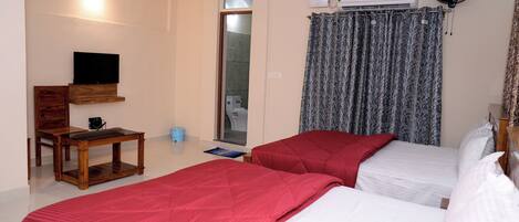 A bedroom with two beds, a wooden table, a TV, and an air conditioning unit.