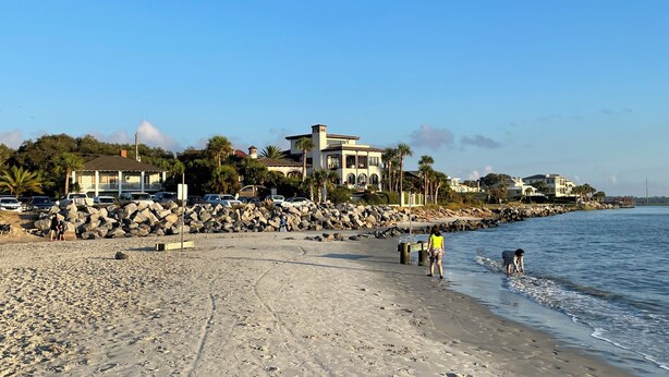 A beach with a rocky shoreline, a pier, and a row of houses in the background. - Easy Beach Stay For Families + King Bed + Bikes + Pool! (St. Simons Island)