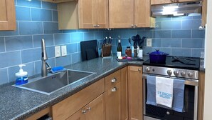 A kitchen with wooden cabinets, a granite countertop, a stainless steel sink, a stove, and a blue tiled backsplash. - Easy Beach Stay For Families + King Bed + Bikes + Pool! (St. Simons Island)