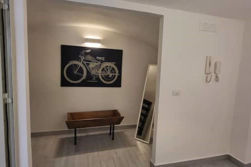 Un pasillo con un cuadro de una bicicleta en la pared, un banco y un espejo apoyado en la pared.