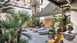 A sunlit outdoor patio with lounge chairs, potted plants, and a stone wall. - ARCUM suites è situato nel cuore di Palermo ,non dovrai usare nessun mezzo  (Palermo)