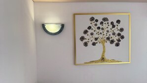 Ein Schlafzimmer mit einem Bett, einer Wandleuchte und einem Bilderrahmen mit einem Baum.
