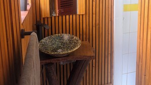 Ein Badezimmer mit Holzvertäfelung, einem runden Waschbecken mit Mosaikschale, einem Spiegel und einer Tür mit gelbem Streifen.