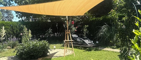 A garden with a wooden easel, a hammock, and a large shade sail.