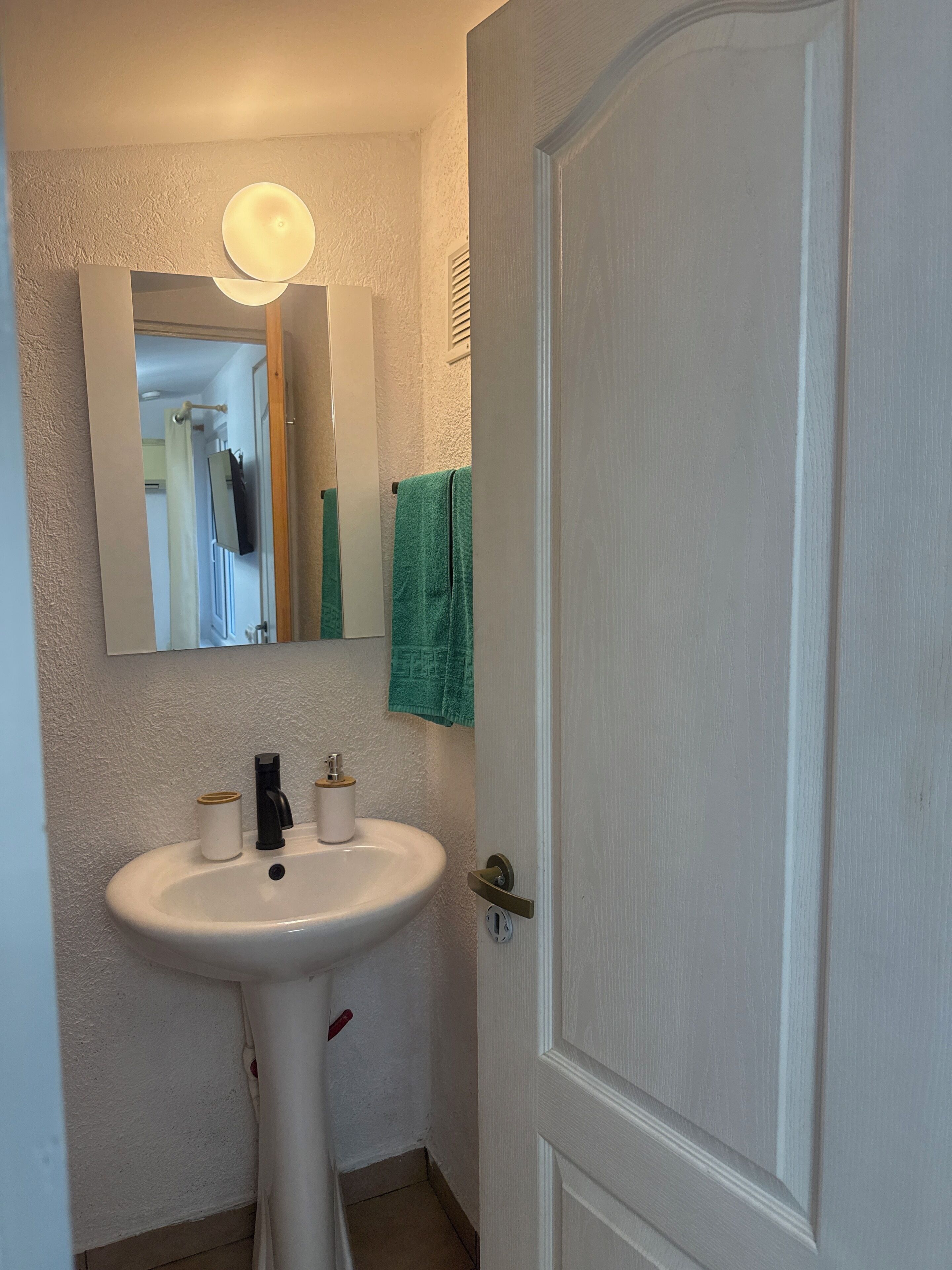 A bathroom with a white sink, a mirror, and a green towel hanging on the wall.
