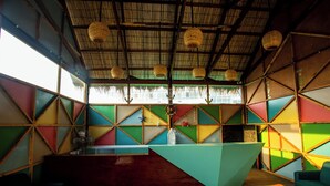 A room with a geometric wall design, a reception desk, a wooden table, and a hanging basket. - Anchor Eco Resort & Spa (Cox's Bazar)