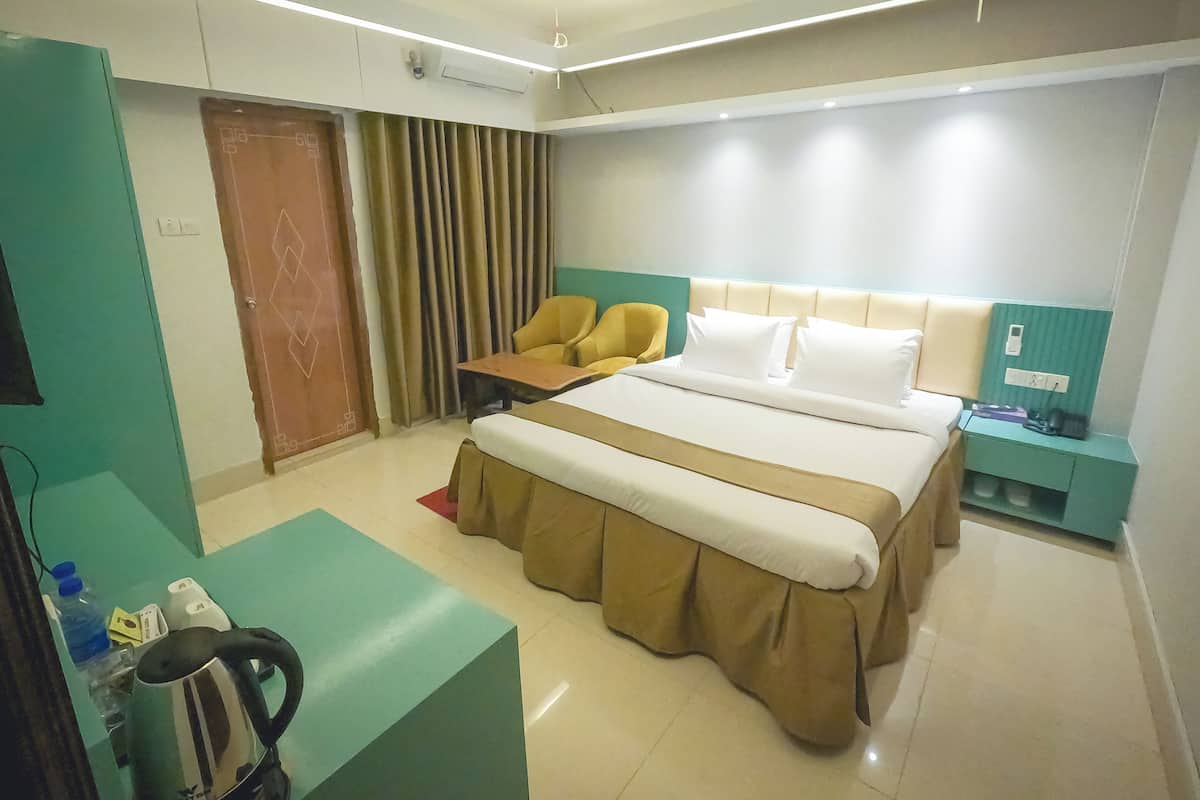 A hotel room with a bed, a desk, a chair, a nightstand, and a kettle.