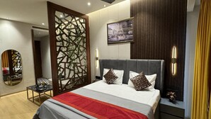 A modern bedroom with a large bed, a ceiling fan, a decorative wall panel, and a framed picture on the wall. - Luxury Deluxe Suite by Gt Studios (Greater Noida)