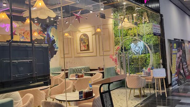 A cafe with a glass front, interior seating, and a neon sign. - Luxury Deluxe Suite by Gt Studios (Greater Noida)