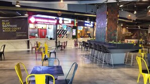 A food court with yellow and blue chairs, a Galaxy Blue Sapphire sign, and a food court sign on the 4th floor. - Luxury Deluxe Suite by Gt Studios (Greater Noida)