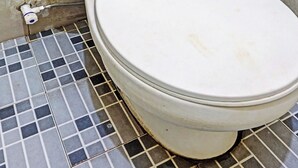 A toilet with a white seat and lid, positioned against a wall with beige tiles. - Capital O 93936 Tower Mahakam by Moii Kingdom (Cikarang)