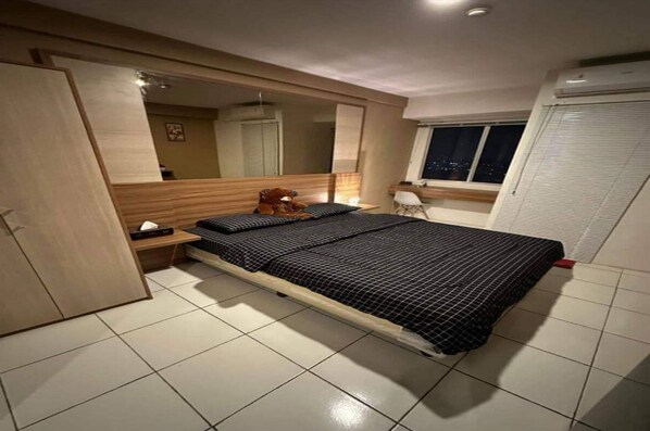 A bedroom with a bed, a bedside table, a mirror, a wardrobe, and a window. - Capital O 93936 Tower Mahakam by Moii Kingdom (Cikarang)