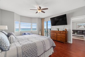 Relax in this serene bedroom with a large bed, wooden dresser, and flat-screen TV, plus a balcony offering ocean views.