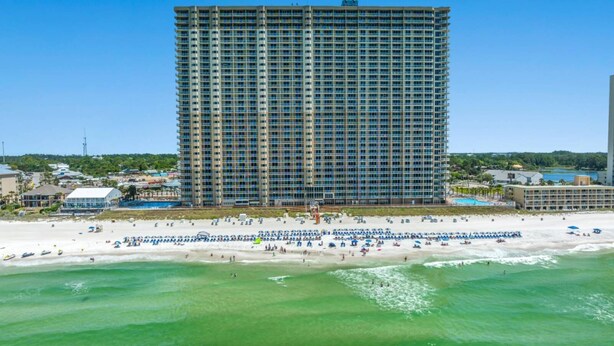 Un grand hôtel à plusieurs étages, une plage au premier plan et un ciel dégagé.