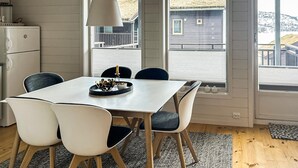 A modern kitchen with a white table, four chairs, a hanging light, and a view of a house through large windows. - Awesome apartment in Tjørhom (Tjørhom)