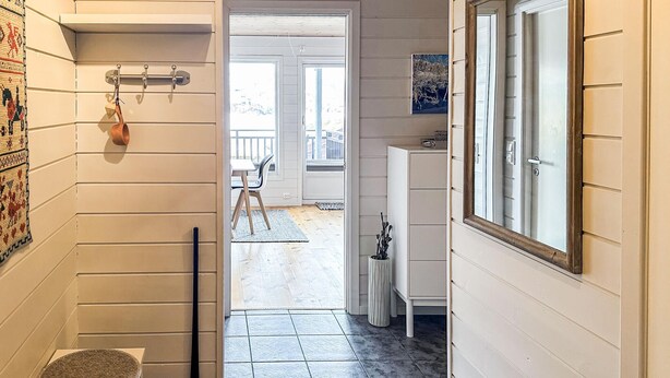 A hallway with a wooden door, a small table with a mat, a potted plant, and a view of an outdoor balcony. - Awesome apartment in Tjørhom (Tjørhom)