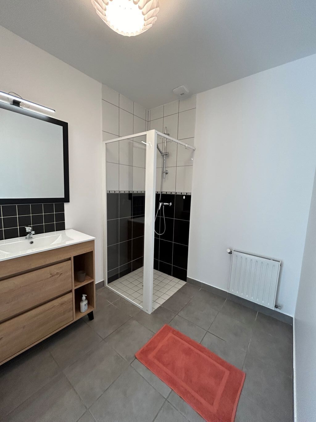 Une salle de bain moderne équipée d’une douche, d’un meuble-lavabo avec miroir et d’un radiateur.