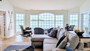 A spacious living room with a large window, a sofa, a chair, and a table with a bowl. - Luxurious 5BR Inlet View Home with Elevator – South Shore Marina (North Bethany)