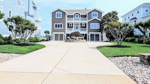 A multi-story residential building with a central entrance, a driveway, and landscaped areas with trees and shrubs. - Luxurious 5BR Inlet View Home with Elevator – South Shore Marina (North Bethany)