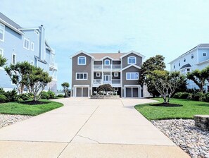Un edifici residencial de diversos pisos amb entrada central, carril d'accés i zones enjardinades amb arbres i arbustos.