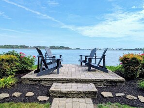 Two Adirondack chairs facing a body of water with a stone-paved deck and a stone border. - Luxurious 5BR Inlet View Home with Elevator – South Shore Marina (North Bethany)