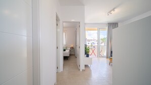 Un pasillo moderno y bien iluminado con vista a un balcón y un vistazo a un dormitorio con cama y mesita de noche.