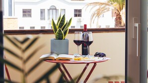 Un balcón con una mesa, una maceta, un libro, dos copas de vino y un casco.