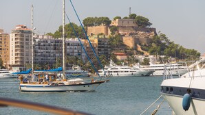 Un port de plaisance avec des bateaux amarrés, un château perché sur une colline et des bâtiments en arrière-plan.