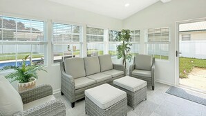 Una habitación soleada con un ventanal grande, muebles de mimbre y una planta en maceta.