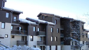 Un immeuble résidentiel à plusieurs étages, doté de balcons et dont le sol est recouvert de neige.