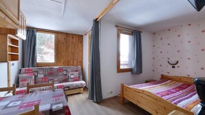 Une pièce de taille modeste, avec un lit en bois, un canapé, une petite table et une fenêtre avec des rideaux.
