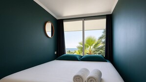 Habitación de hotel con cama, vista al océano y cortinas.